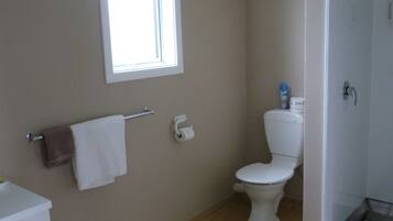 A bathroom with a toilet, a towel rack, a window, and a shower area.