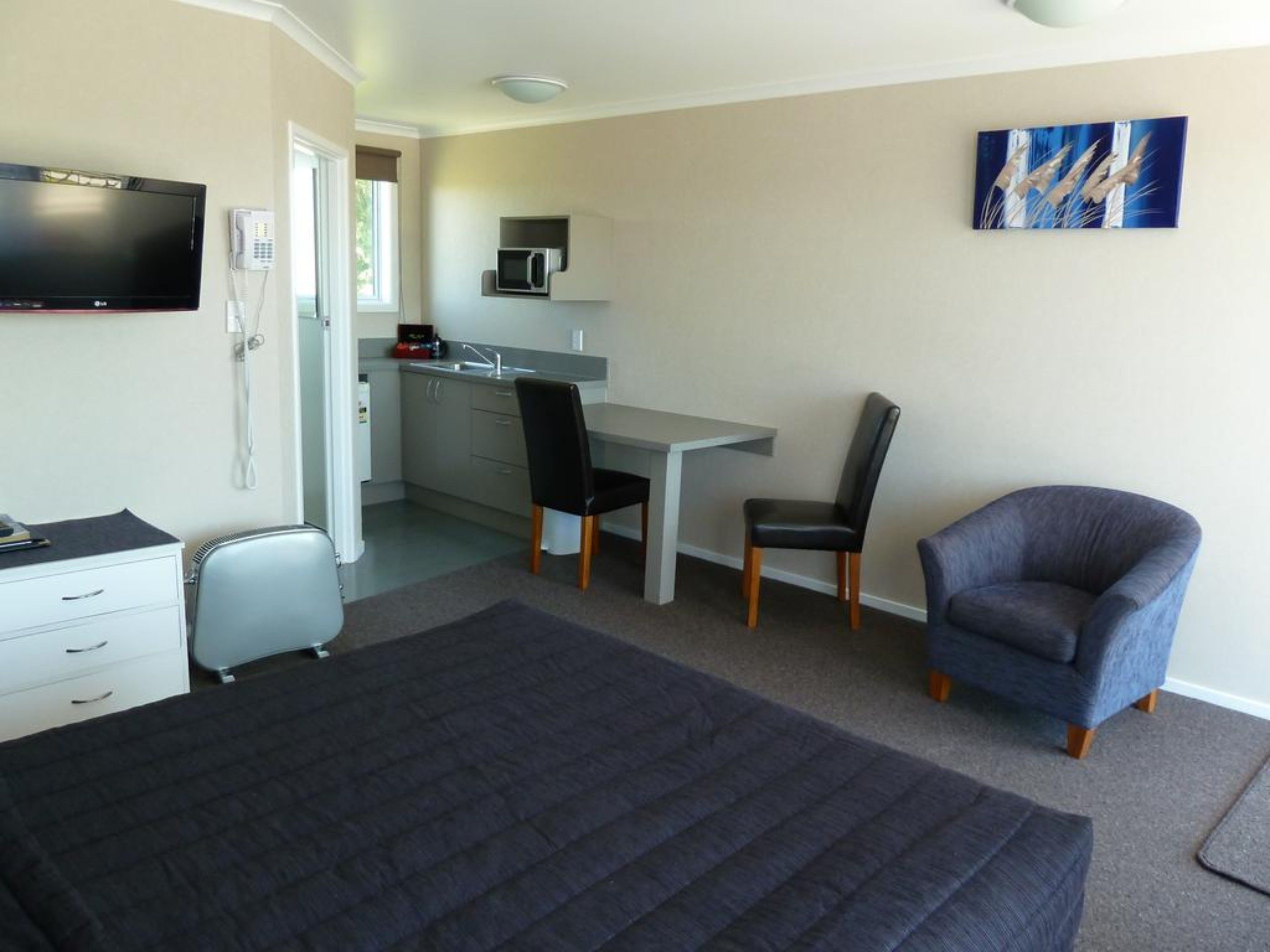Une chambre d’hôtel comprenant un lit, un bureau, deux chaises, une télévision et une kitchenette.