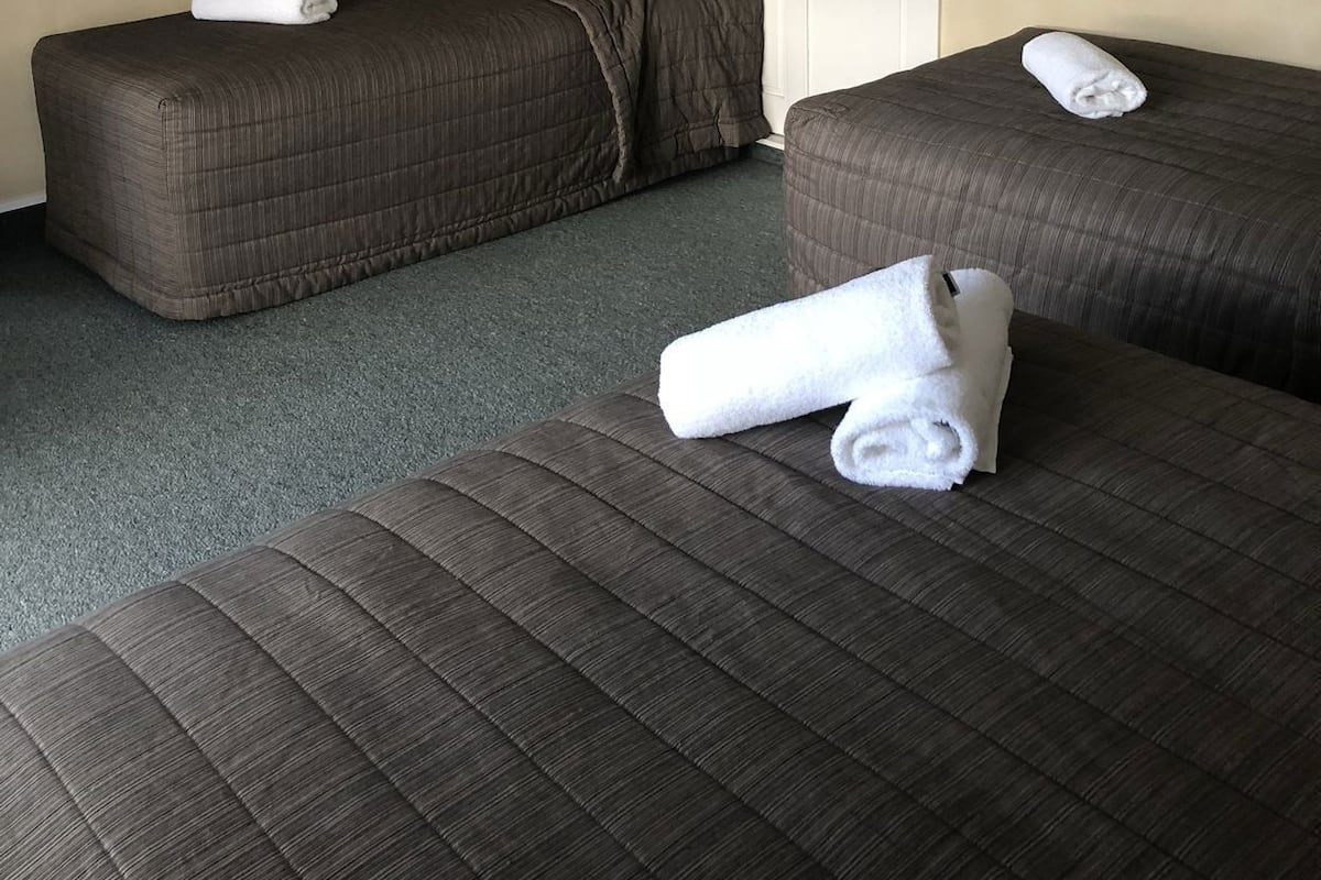 A hotel room with two beds, each with a rolled white towel.