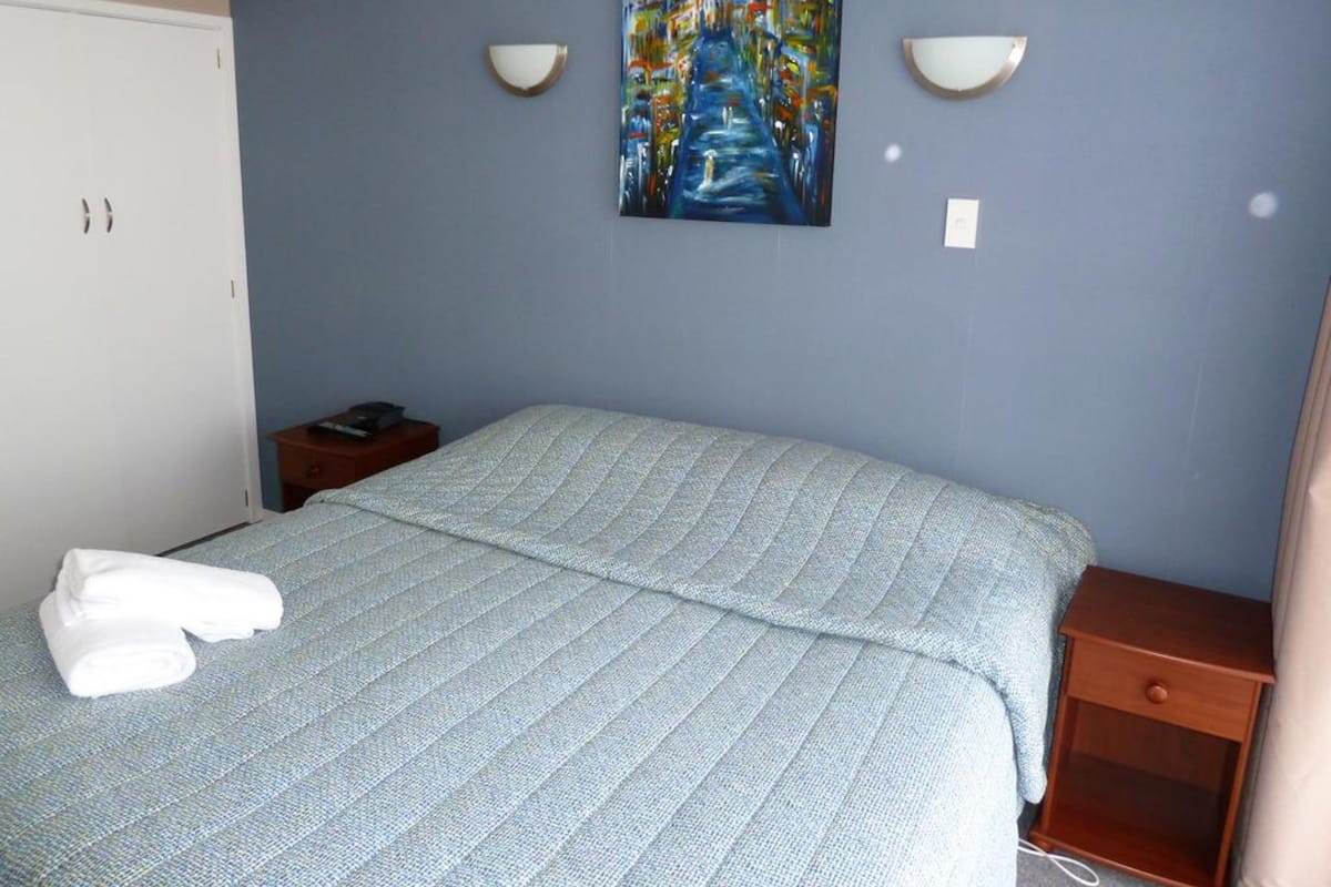 A bedroom with a bed, a nightstand, a painting on the wall, and a wardrobe.