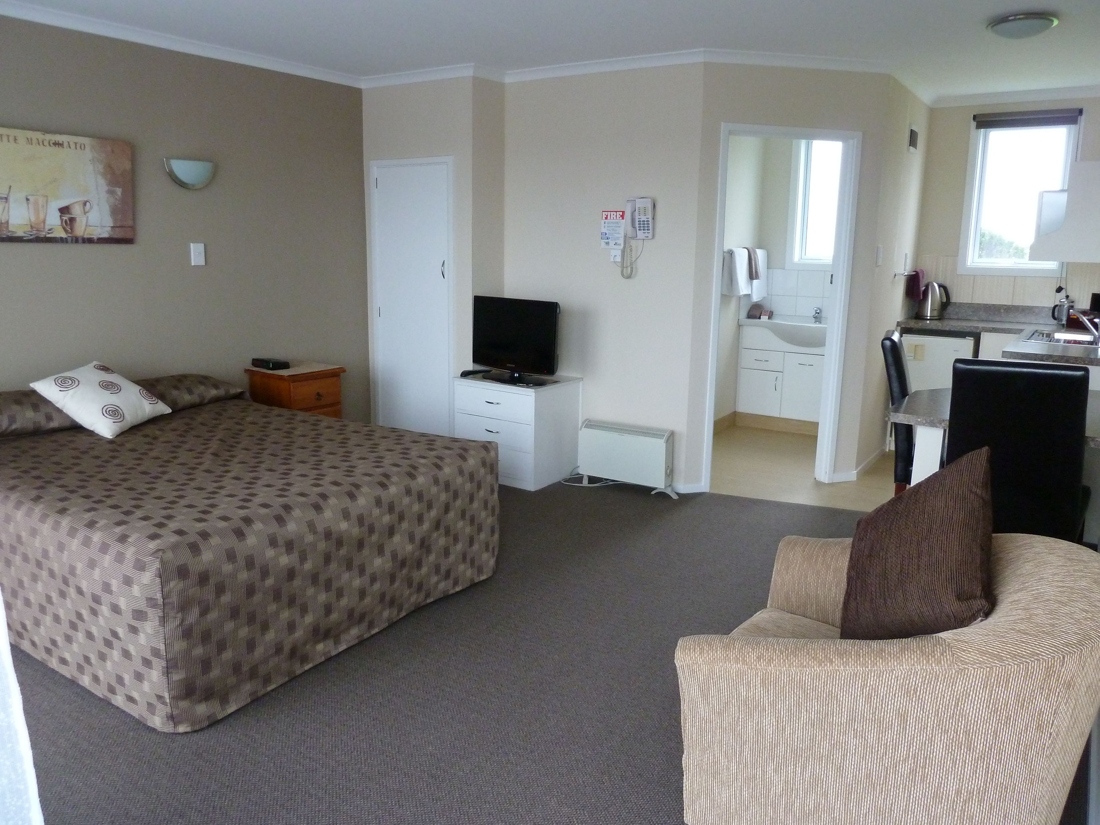 A hotel room with a bed, a TV, a desk, and a kitchenette.