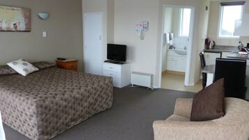 A hotel room with a bed, a TV, a desk, and a kitchenette.