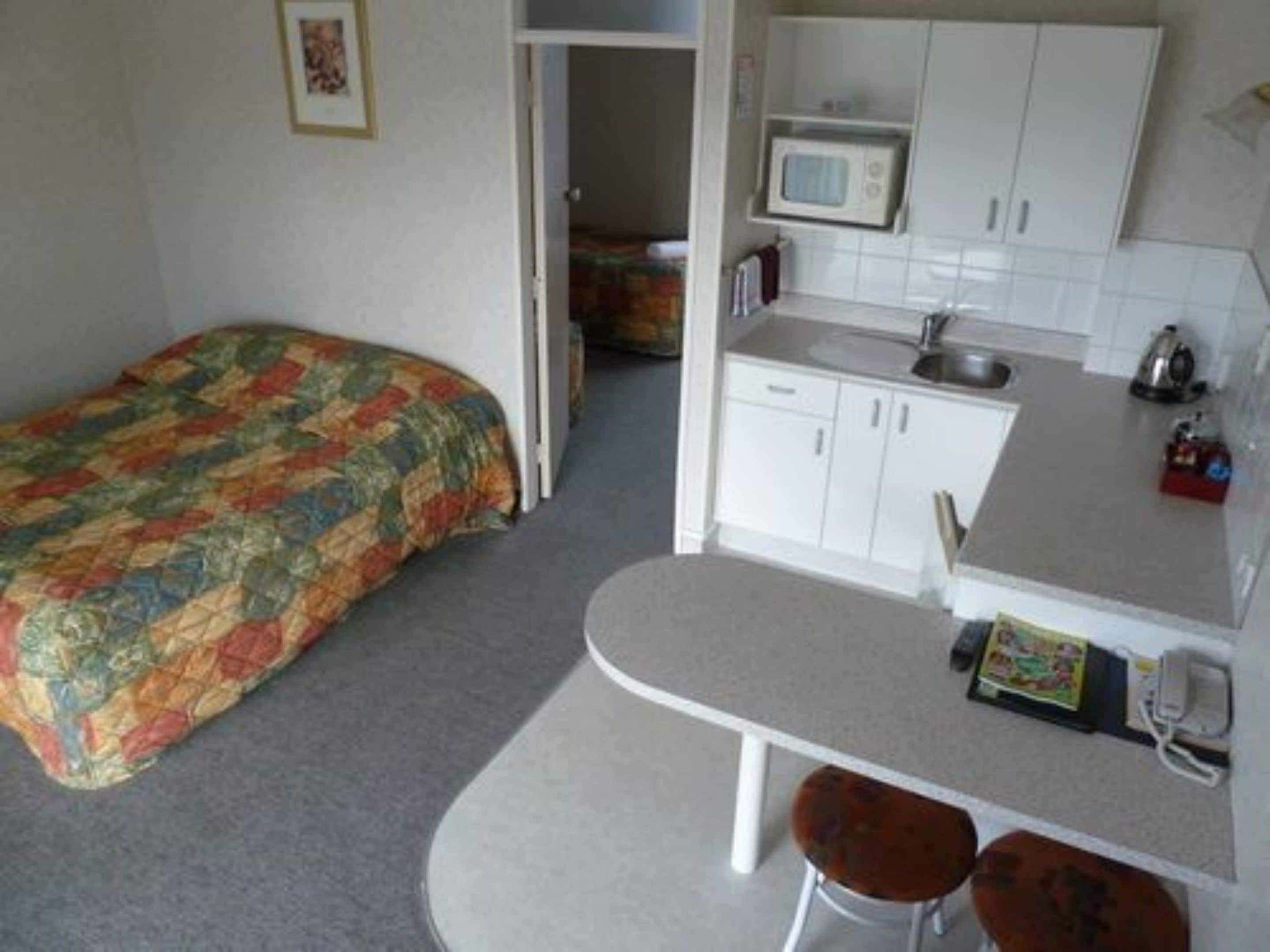 A compact room with a bed, kitchenette, and a small dining area.