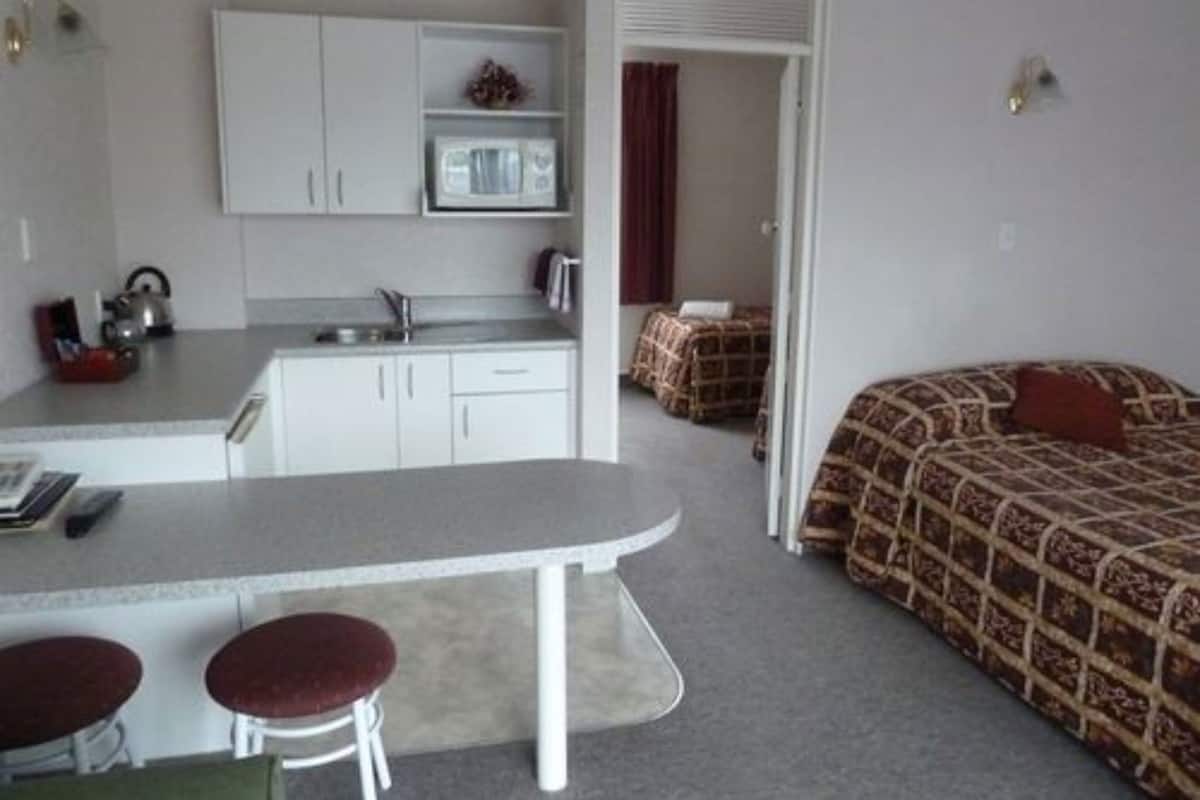A compact room with a kitchenette, a bed with patterned bedding, and a small seating area with stools.