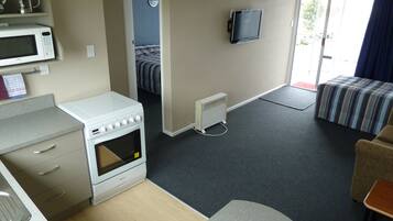 A compact room with a kitchenette, a bed, a TV, and a view of the outdoors.