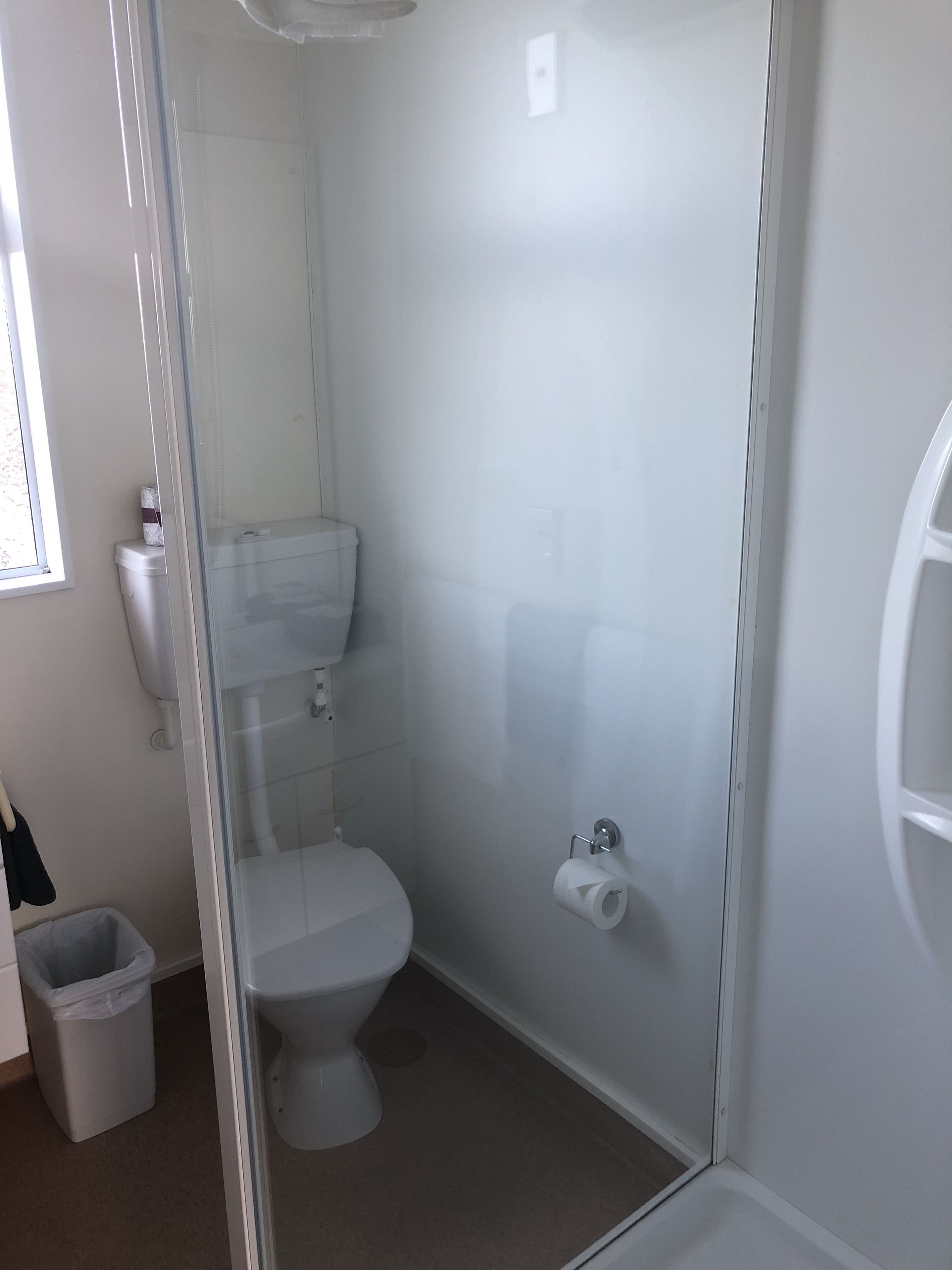 A bathroom with a toilet, a glass shower enclosure, and a trash bin.