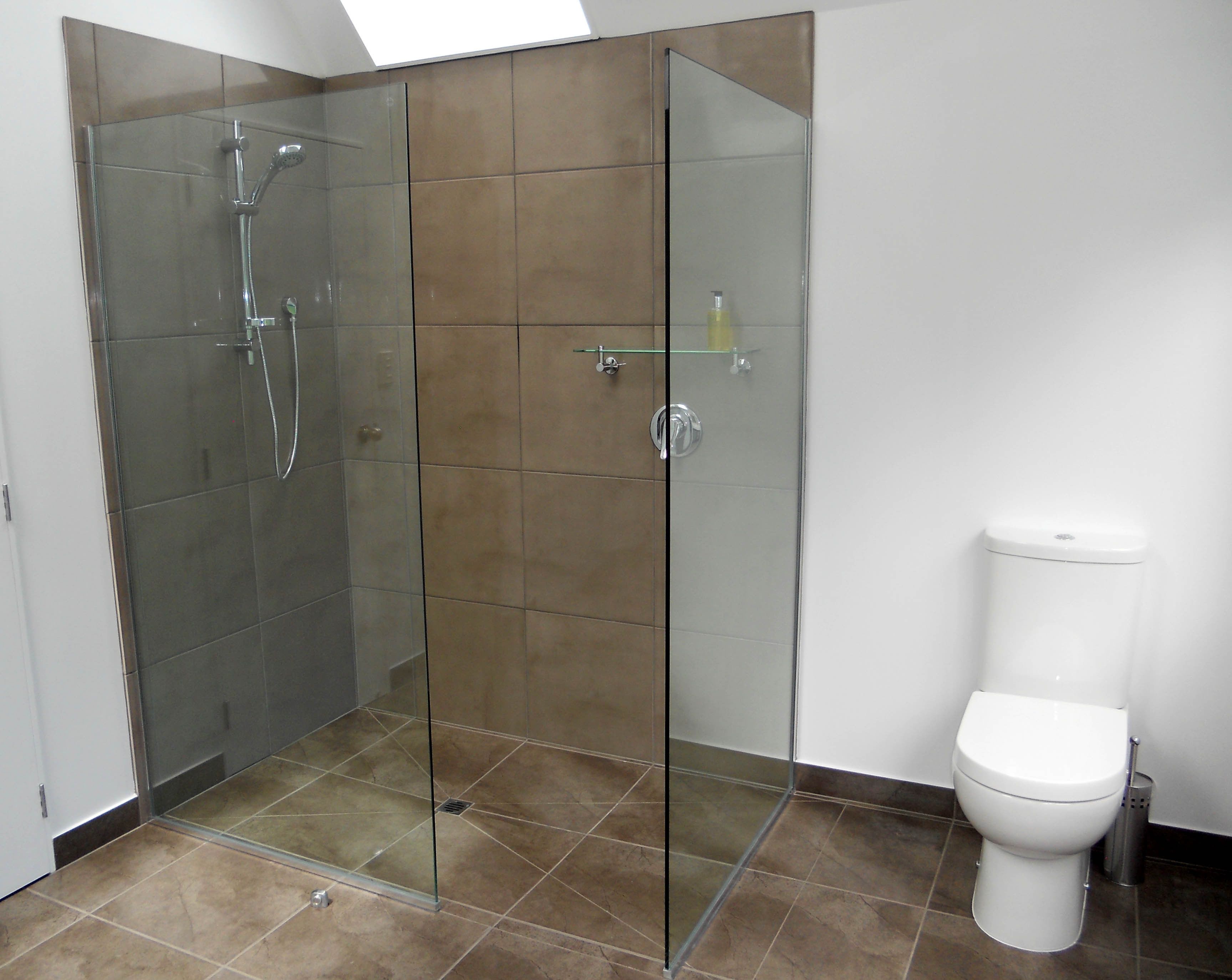 Ein modernes Badezimmer mit einer gläsernen Duschkabine, einer Toilette und einem Glasregal.