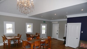 A spacious dining area with wooden tables and chairs, a chandelier, and large windows. - Lupton Lodge (Glenbervie)