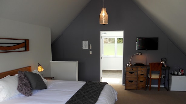 A bedroom with a bed, a desk, a chair, a TV, and a door leading outside. - Lupton Lodge (Glenbervie)
