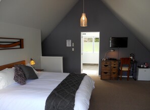 Een slaapkamer met een bed, een bureau, een stoel, een televisie en een deur die naar buiten leidt.