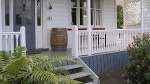 A white house with a blue door, a wooden barrel, and a porch with white railings. - Lupton Lodge (Glenbervie)