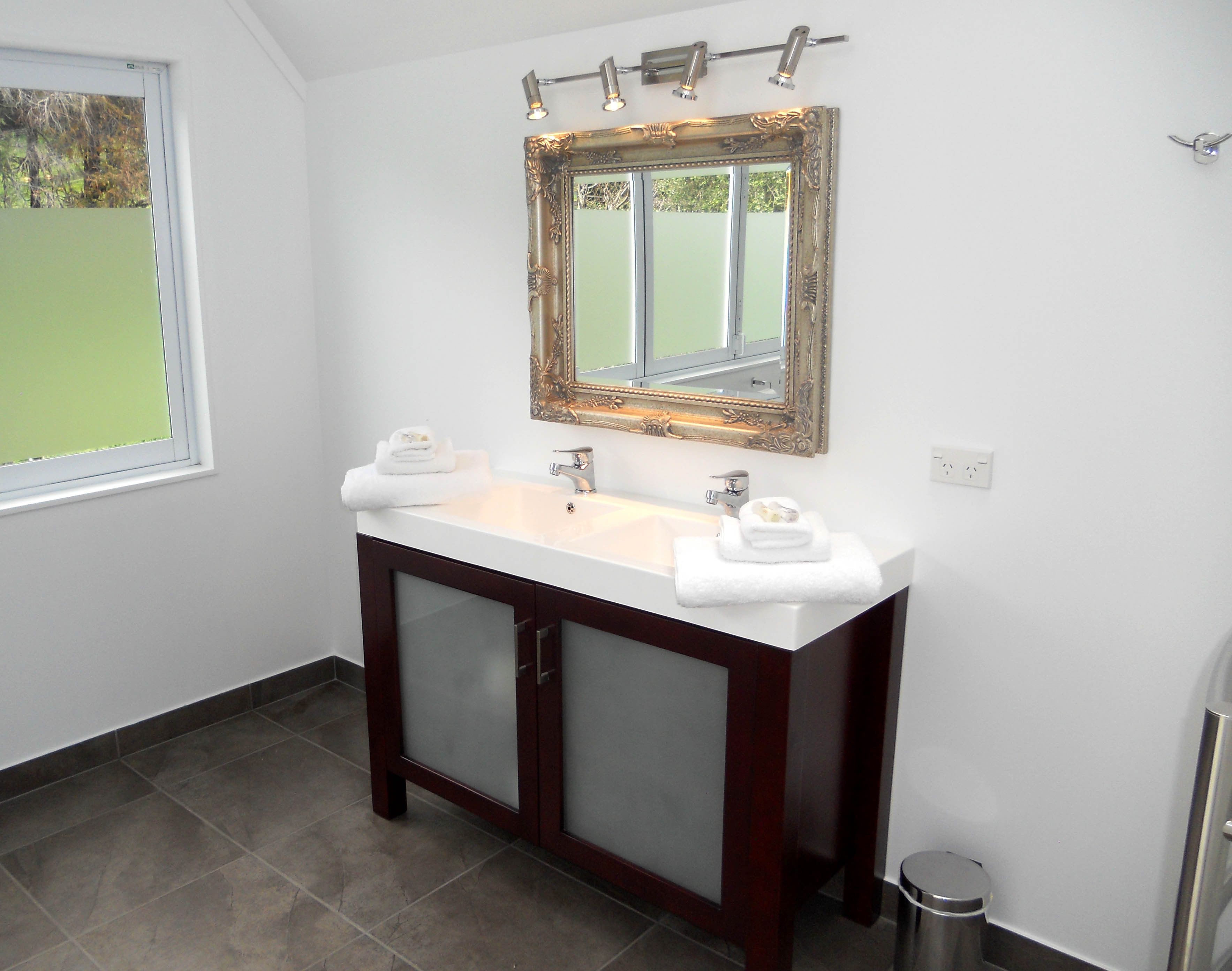 A bathroom with a white sink, two mirrors, and a window.