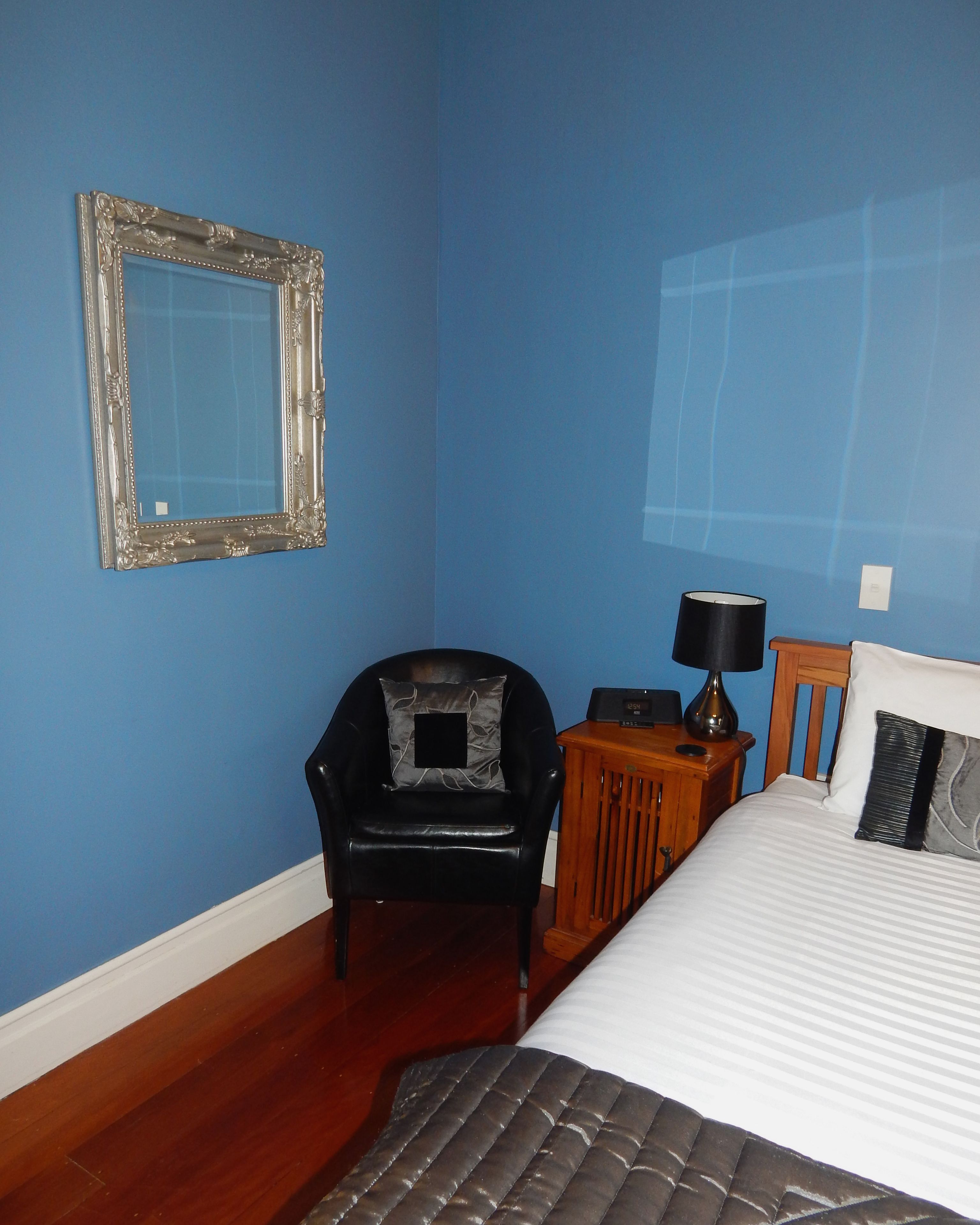 Quarto com cama, cadeira, mesa de cabeceira, abajur e espelho na parede.