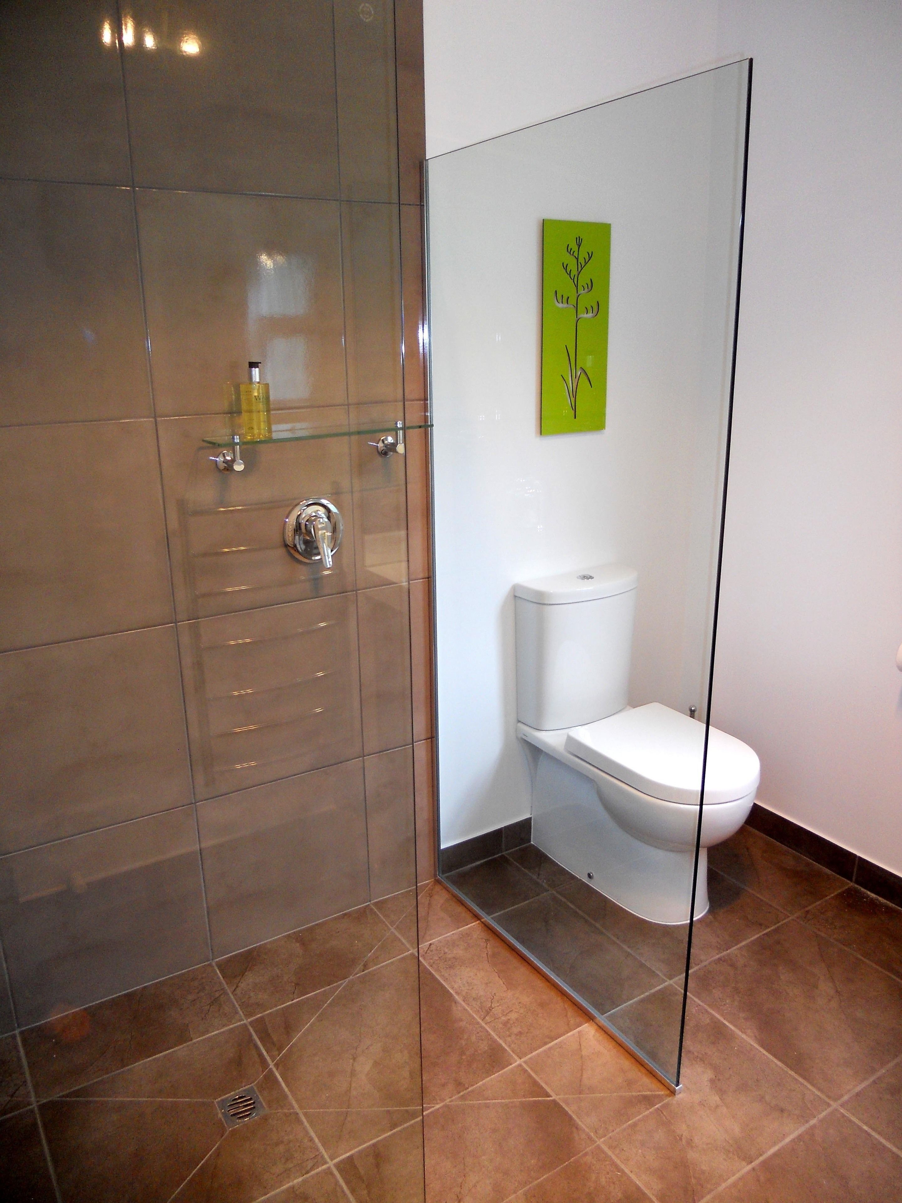 A modern bathroom with a glass shower enclosure, a white toilet, and a green abstract wall art piece.