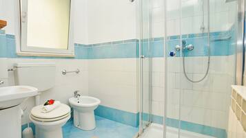 A bathroom with a glass-enclosed shower, a toilet, a bidet, and a sink.