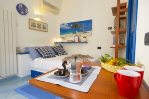 Een gezellige woonkamer met een bank, een bijzettafeltje met een dienblad, een schilderij van een strandgezicht en een mand met fruit.