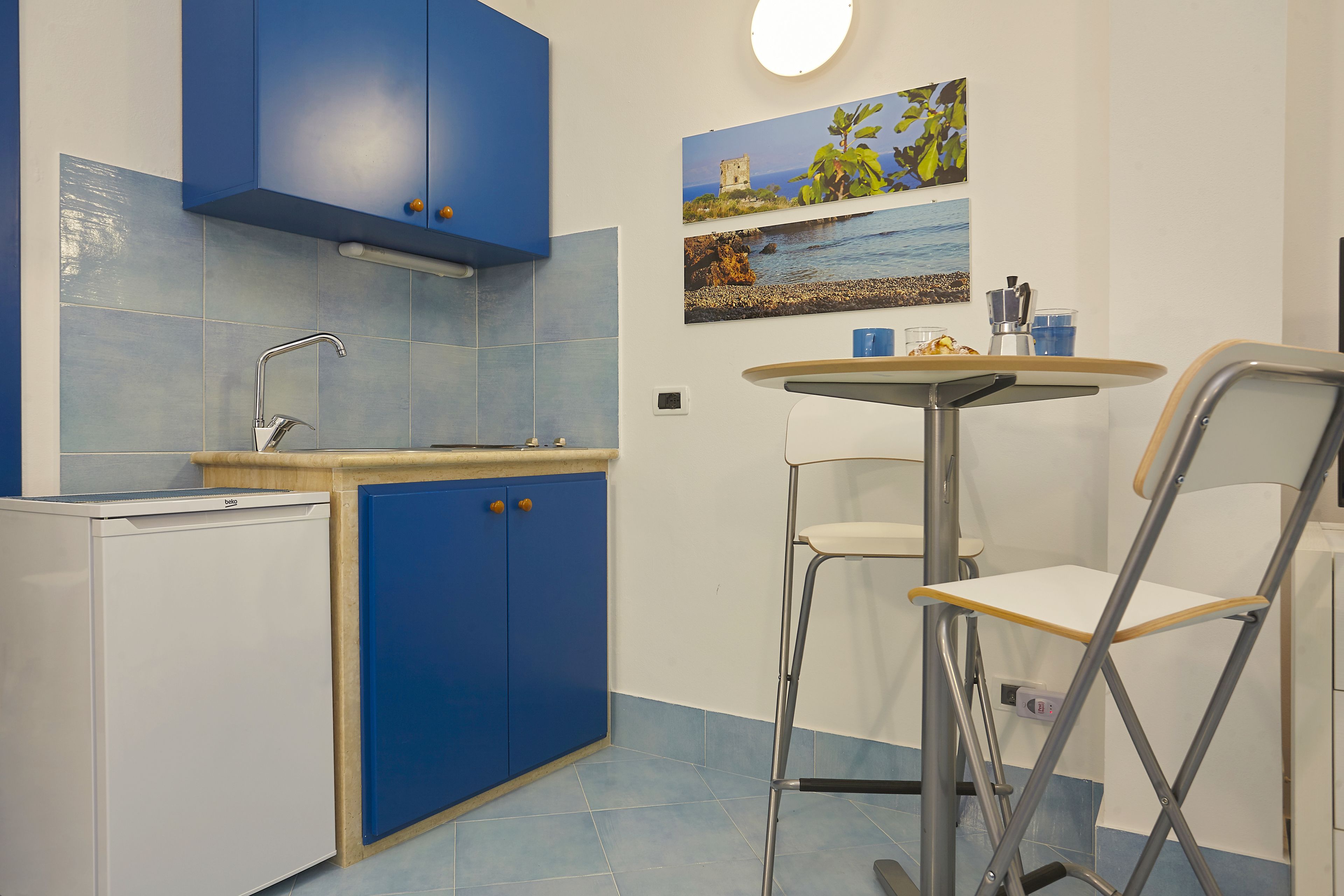 A compact kitchen with blue cabinets, a small sink, and a dining area with a table and two chairs.