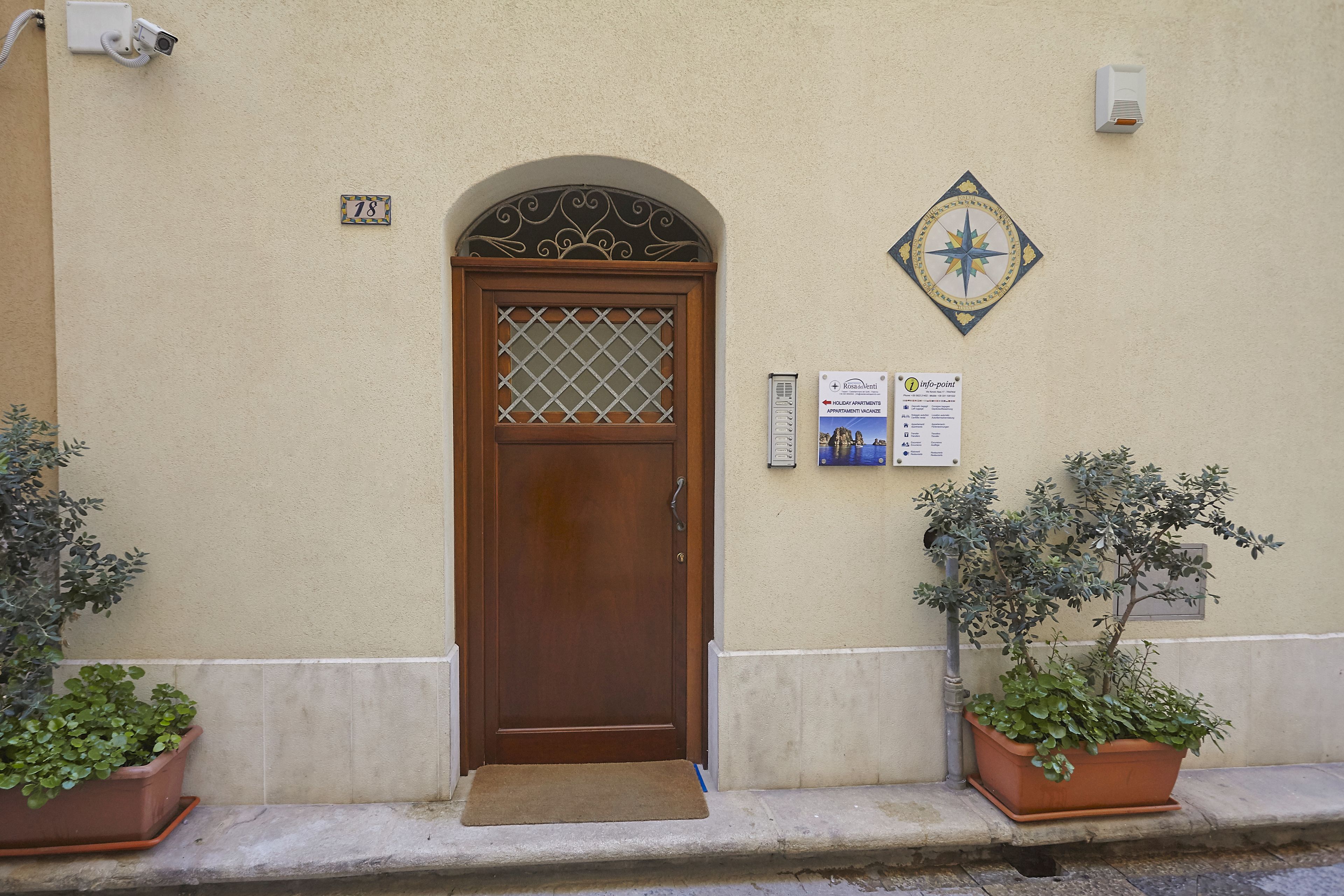 A beige building with a wooden door, a number plate, and two potted plants on the sidewalk.