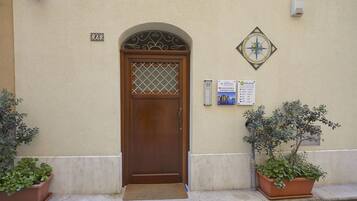 A beige building with a wooden door, a number plate, and two potted plants on the sidewalk.