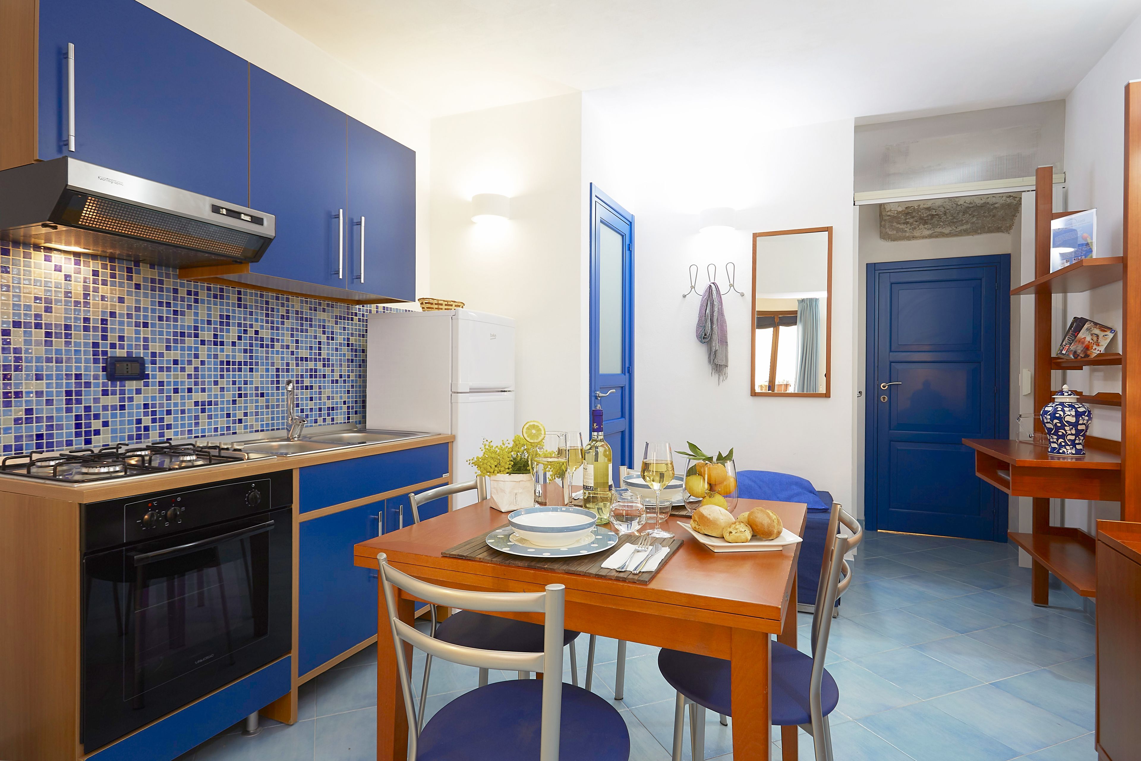 Una cucina compatta con mobili blu, un fornello a gas e un'area pranzo con tavolo apparecchiato per due.