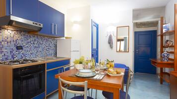 Una cucina compatta con mobili blu, un fornello a gas e un'area pranzo con tavolo apparecchiato per due.