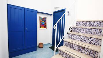 Un corridoio con porte blu, una scala con piastrelle decorate e un'opera d'arte colorata appesa al muro.