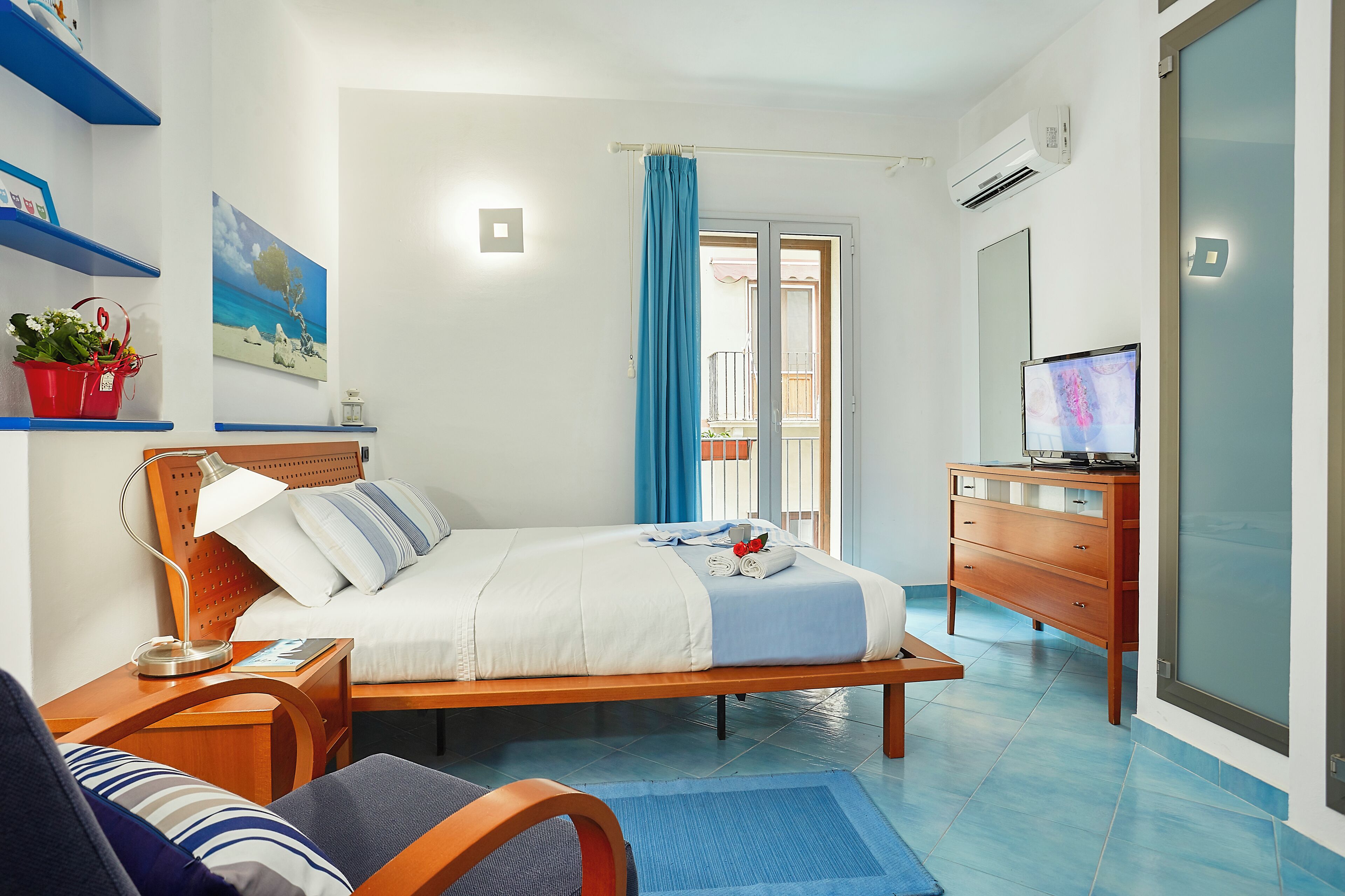 A neatly arranged bedroom with a bed, bedside table, TV, and a view of the balcony.