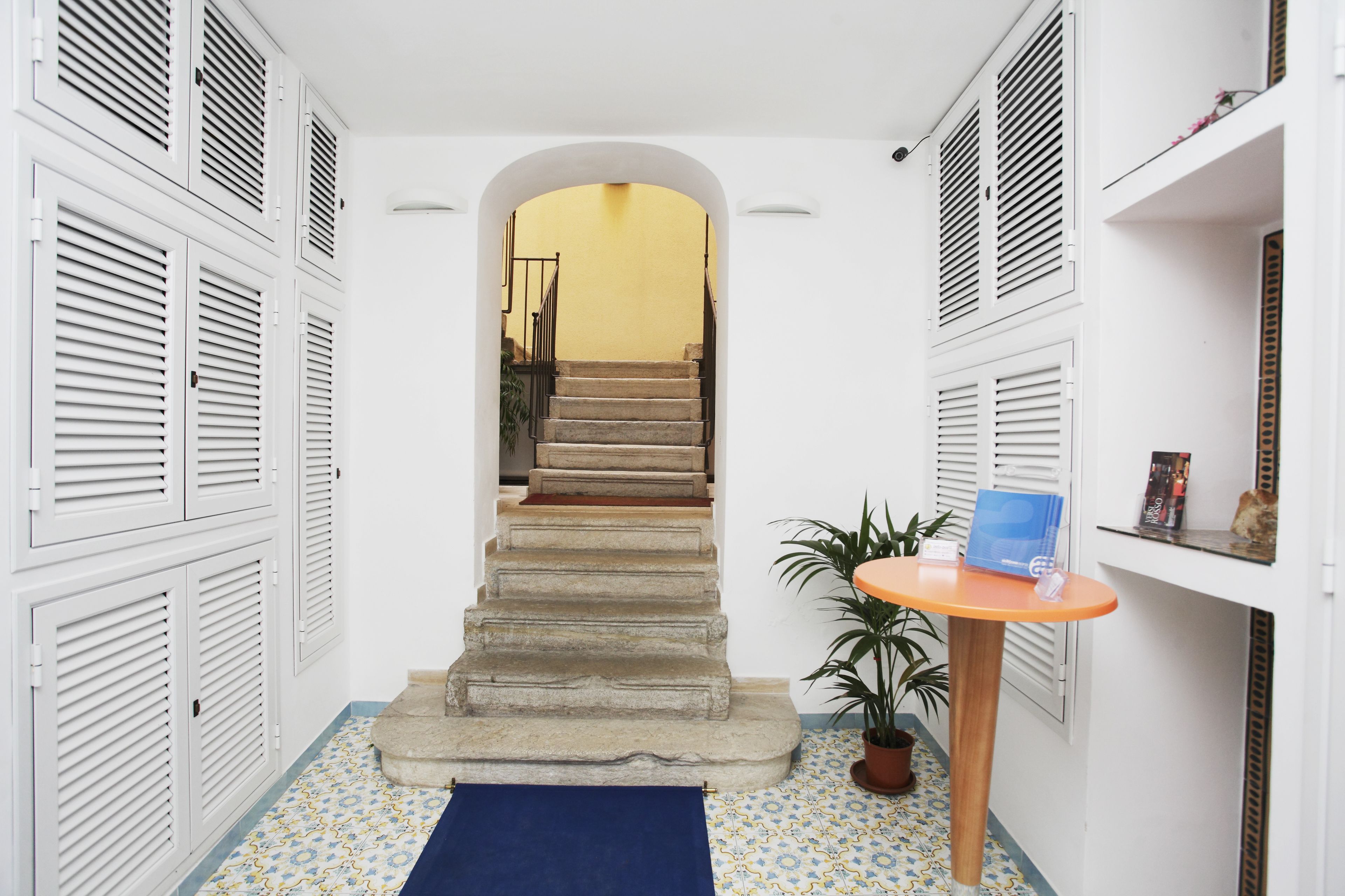 A narrow hallway with a stone staircase leading to a yellow room. There is a small table with a plant and a blue folder on the right.