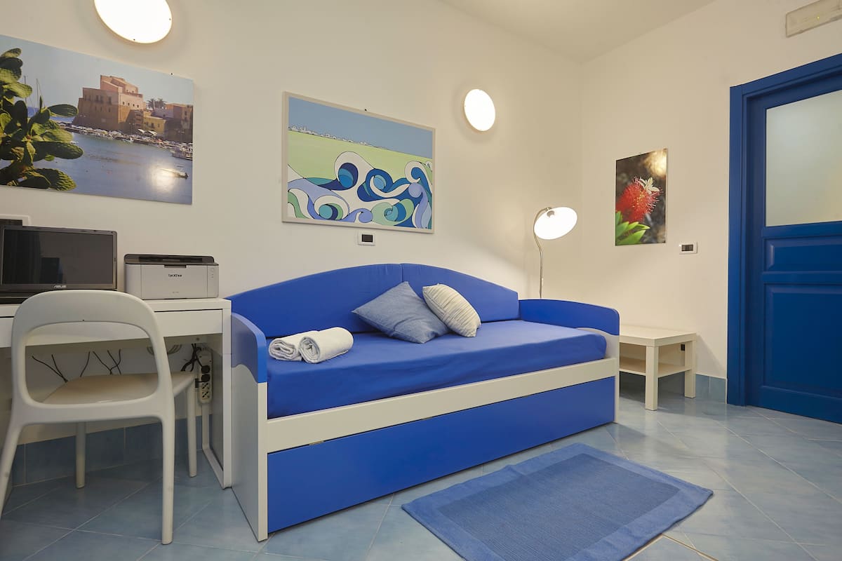 A room with a blue sofa, a desk, a chair, and artwork on the walls.