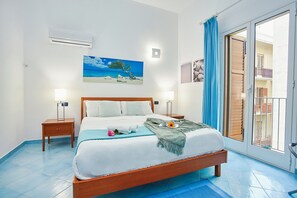 Un dormitorio con cama, mesitas de noche, un cuadro y vistas a través de un ventanal corredero.