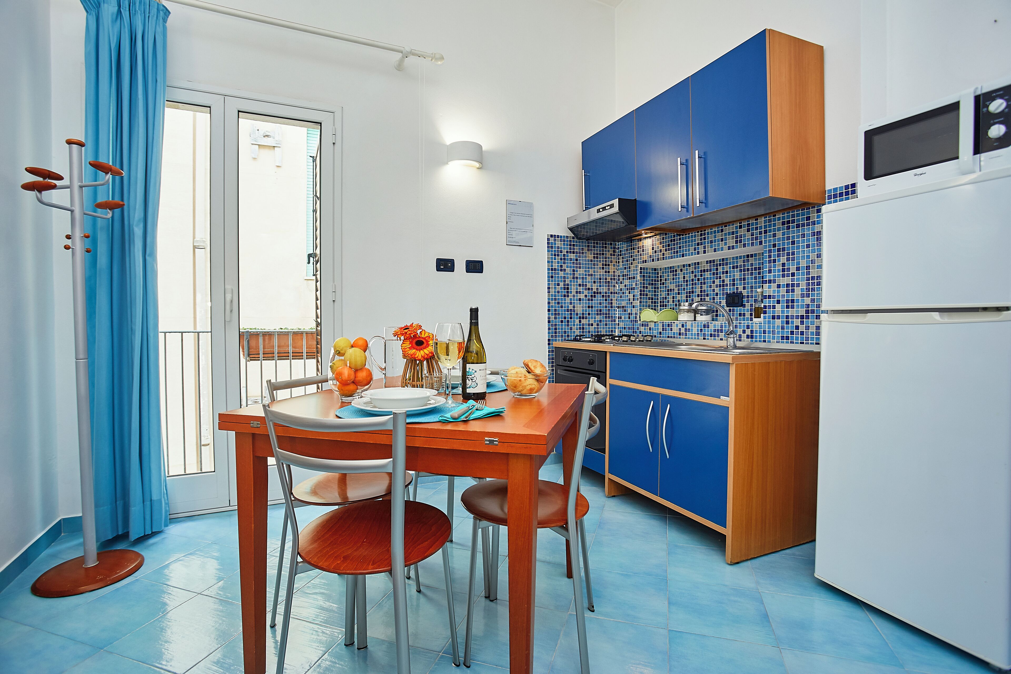 A compact kitchen with blue cabinets, a white refrigerator, and a dining area with a table and chairs.
