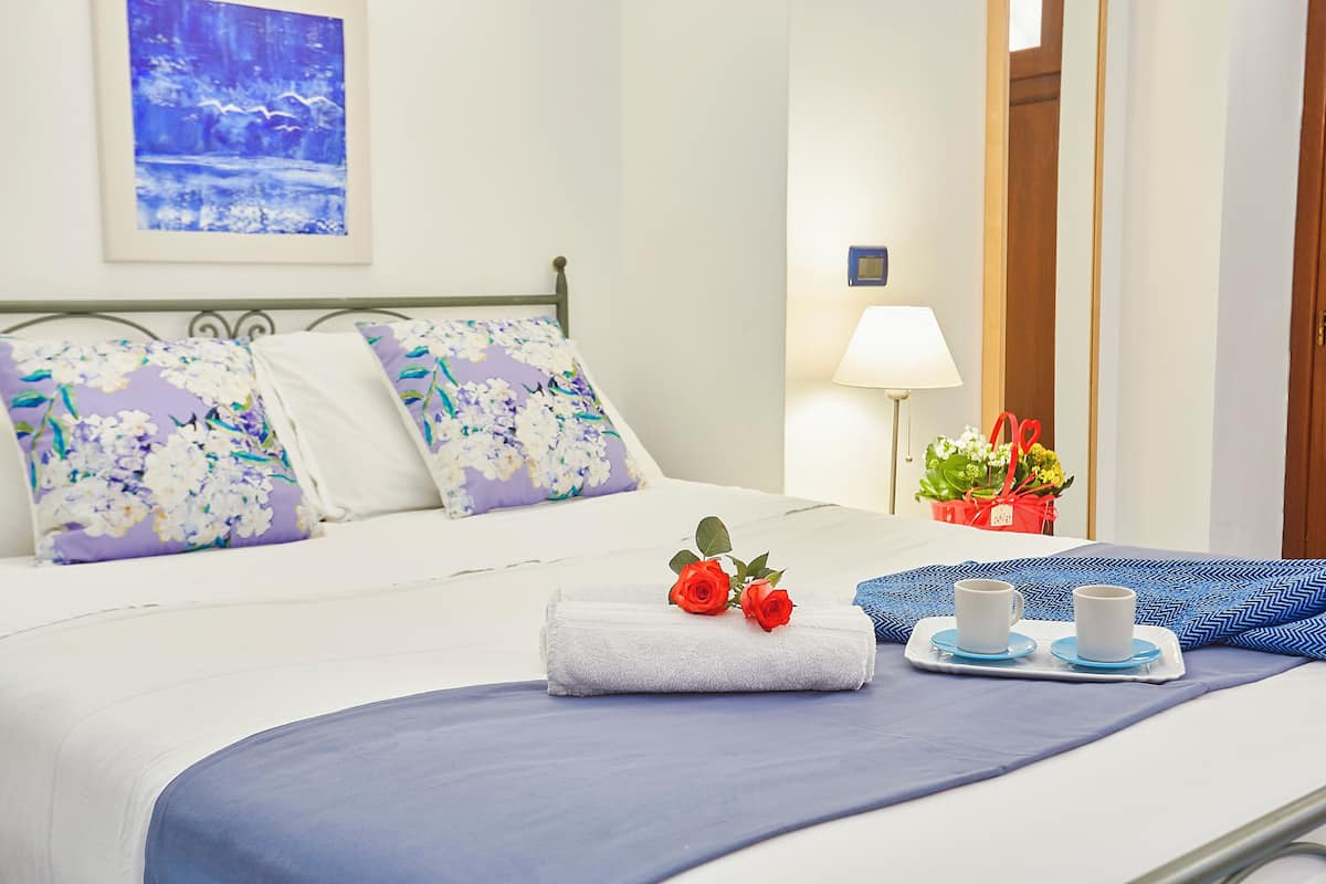 A neatly made bed with floral pillows, a white towel, and two cups on a tray.
