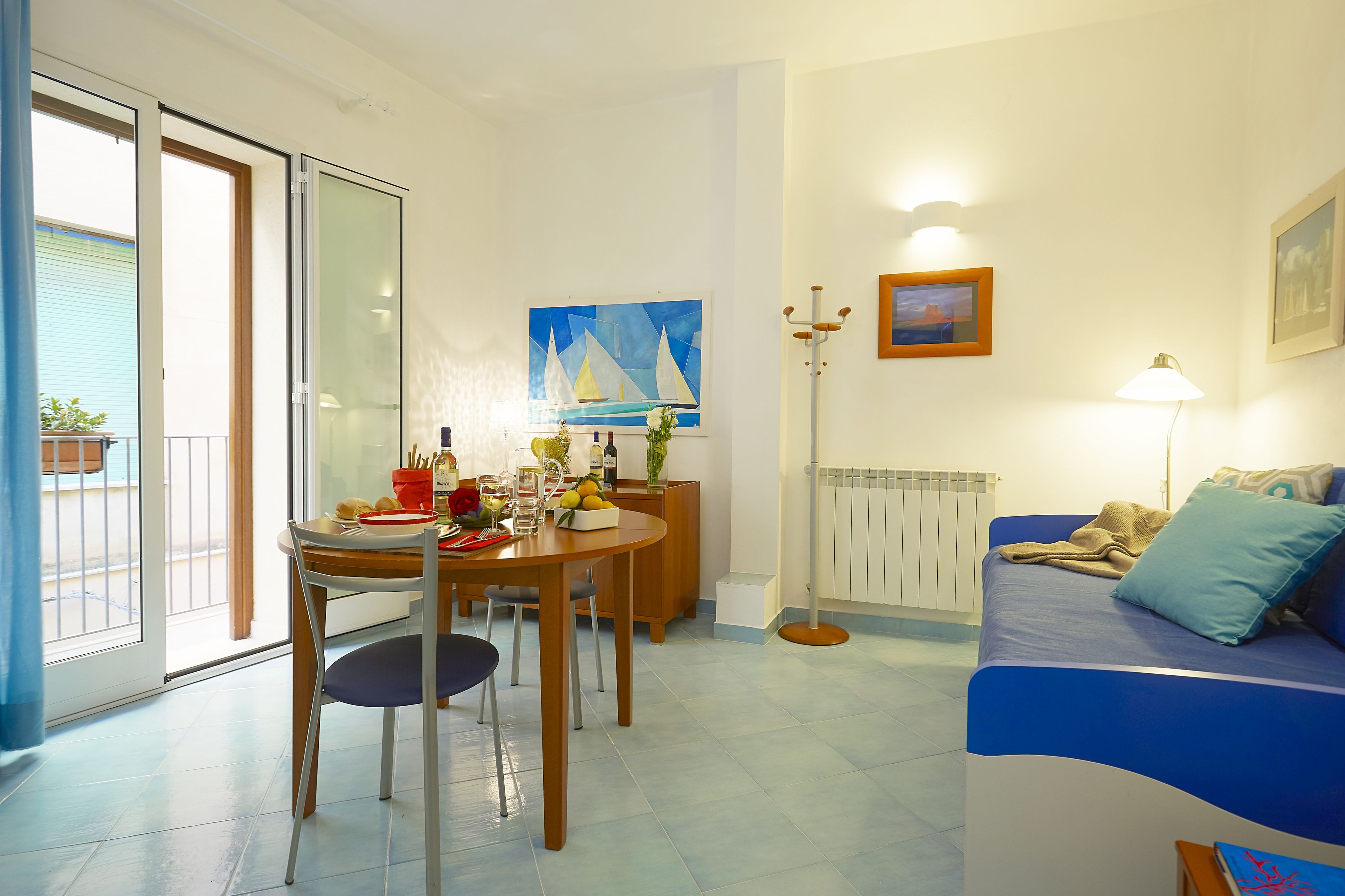 A room with a dining table, chairs, a sofa, a lamp, and artwork on the walls.