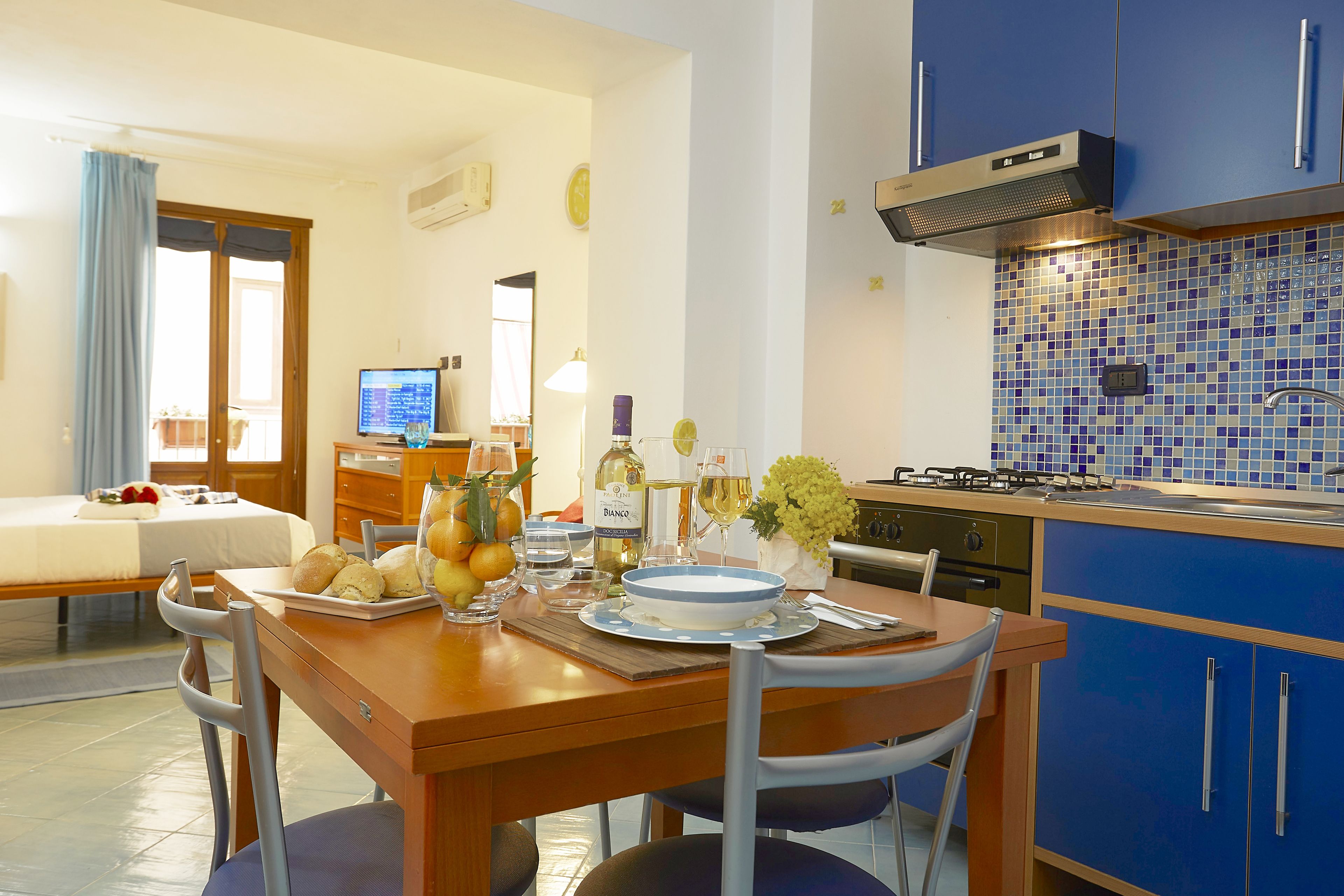 Een moderne keuken met blauwe kastjes, een eettafel gedekt met borden, glazen en een fles.