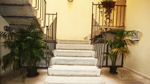 Una escalera de piedra con barandillas de metal, flanqueada por macetas con plantas.