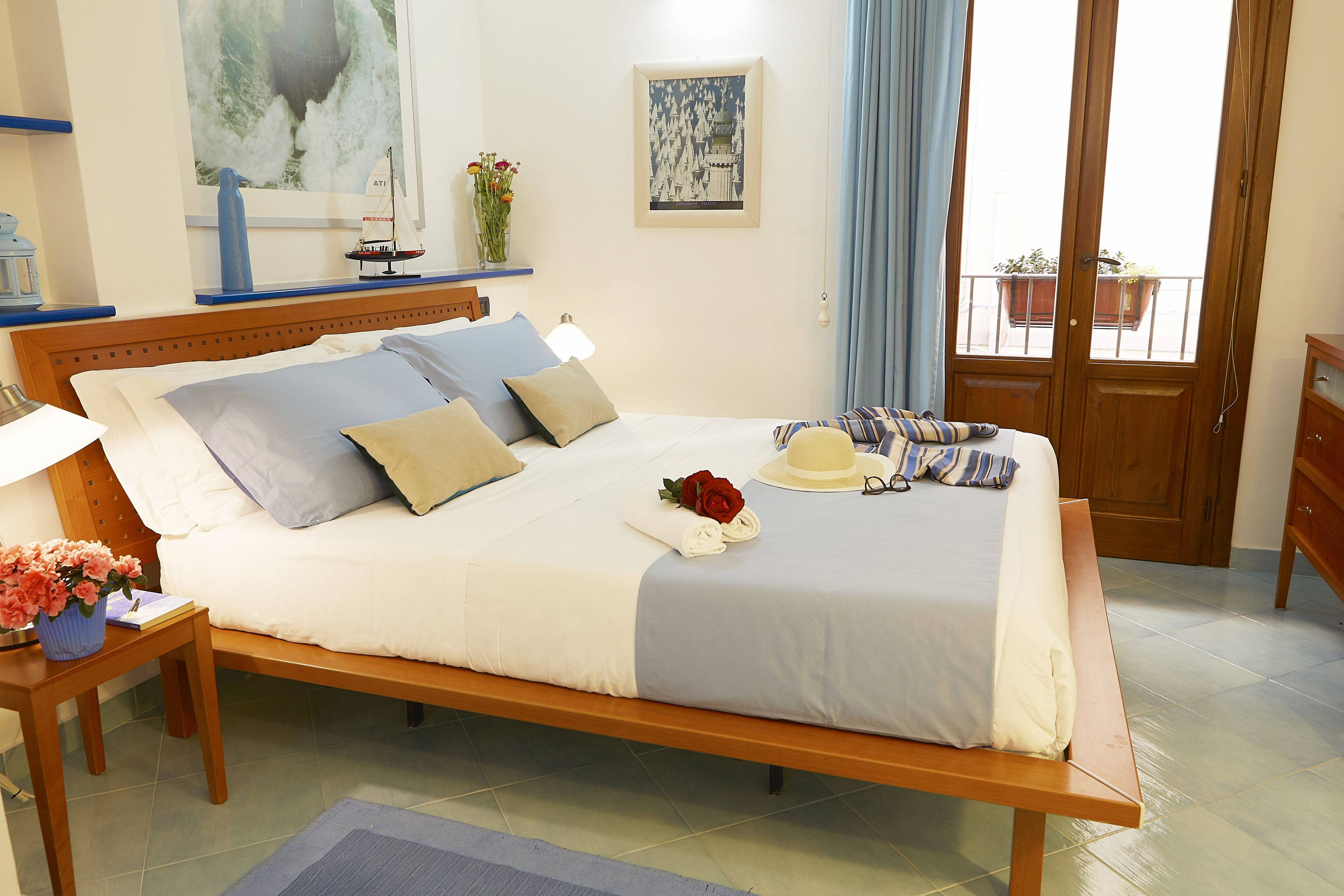 A neatly made bed with a blue and white bedspread, a wooden headboard, and a bedside table with a lamp and a vase of flowers.