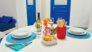 Una mesa de comedor dispuesta con platos, vasos, una botella de vino, pan y una cesta de barras de pan.