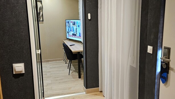 A hallway with a wooden floor, a black wall, and a white door with a curtain. - Hôtel L'Européen (Tarbes)