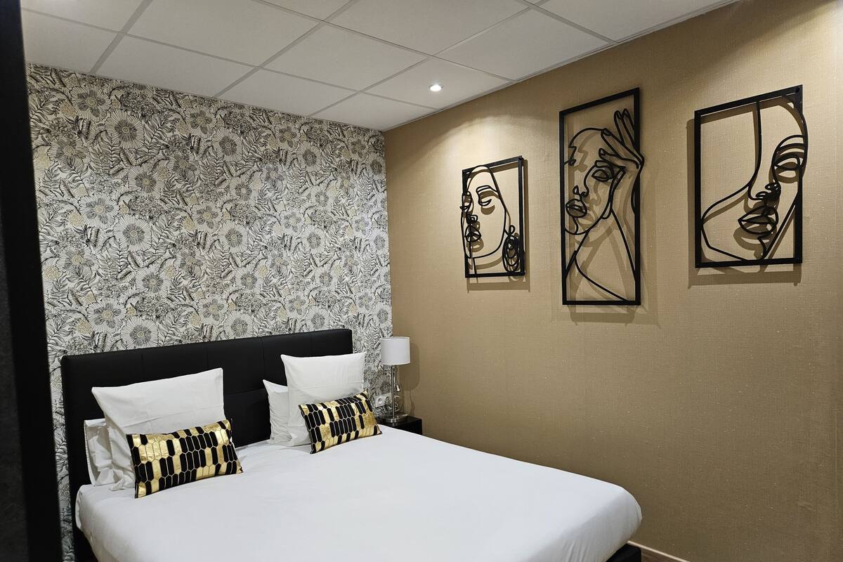 A hotel room with a large bed, a floral wallpaper, and three abstract art pieces on the wall.