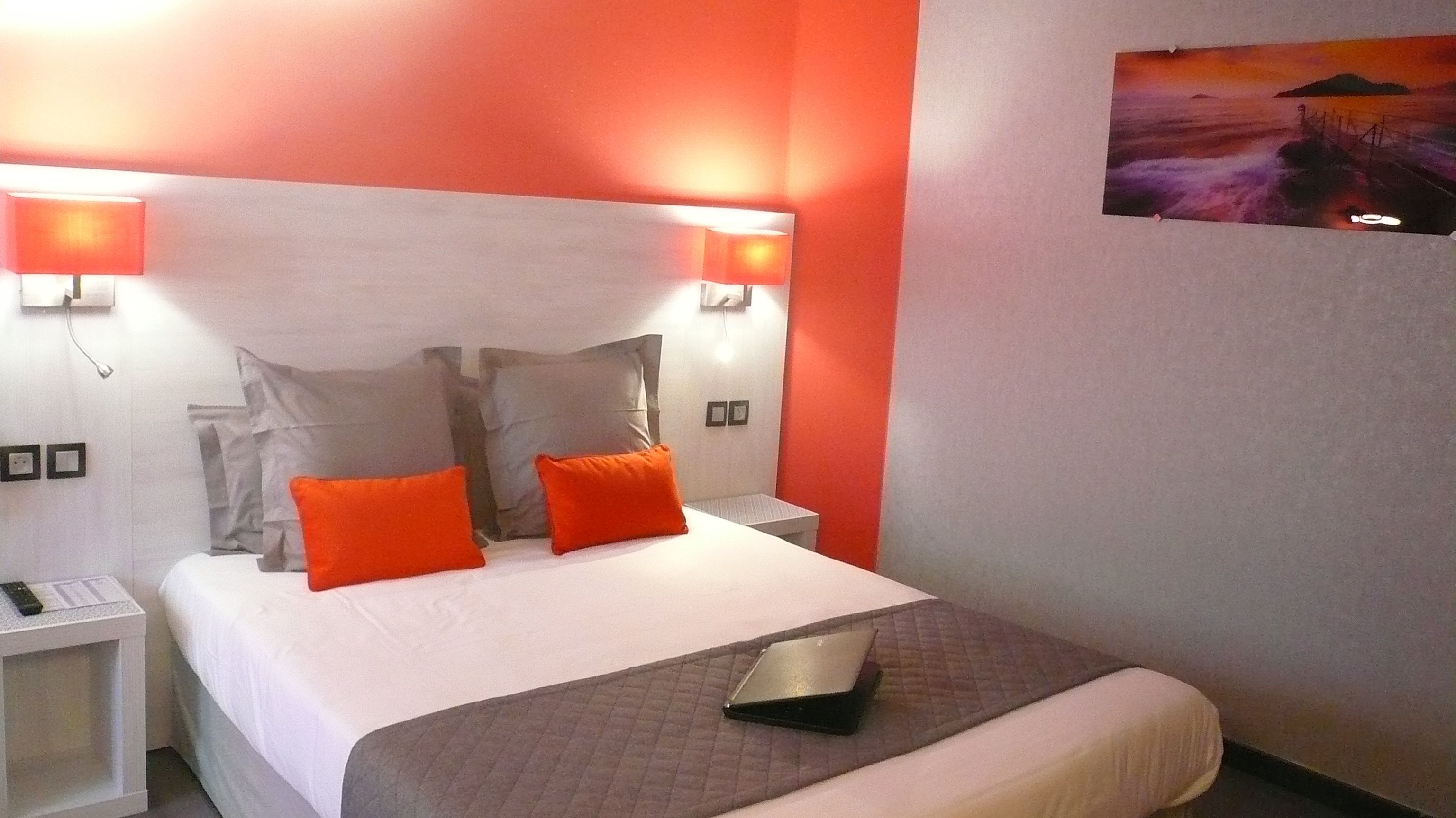 A hotel room with a bed, two nightstands, a laptop, and a painting on the wall.