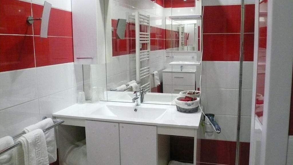 Un baño moderno con un lavamanos blanco, un espejo y paredes con baldosas rojas.