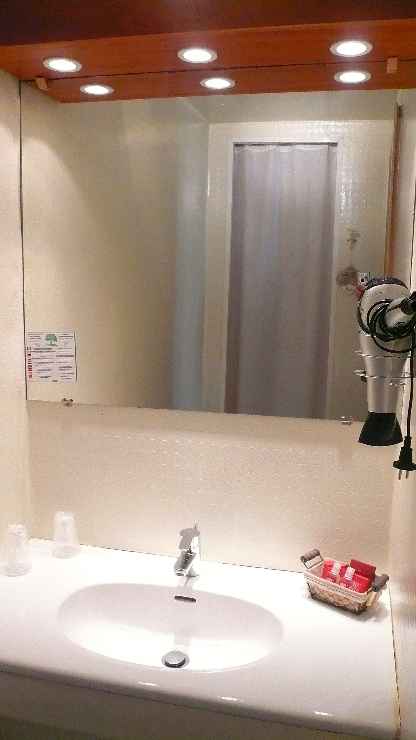 Une salle de bain avec un lavabo blanc, un miroir et un sèche-cheveux fixé au mur.