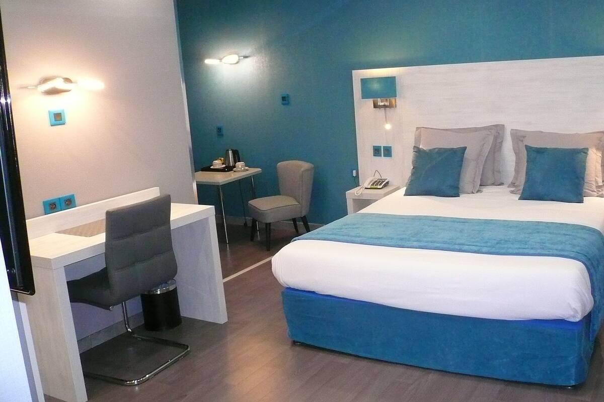 A modern hotel room with a large bed, a desk, a chair, and a small table with a coffee maker.