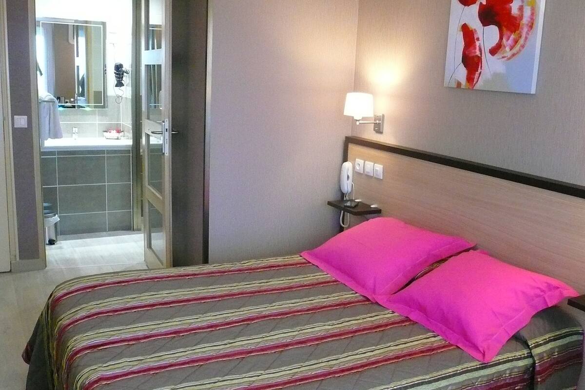 A hotel room with a bed, a nightstand, a telephone, and a bathroom visible through an open door.