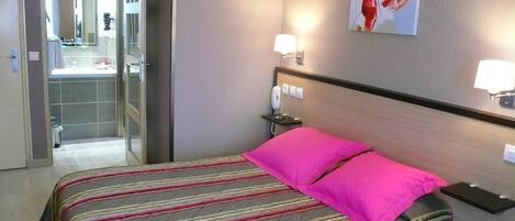 A hotel room with a bed, a nightstand, a telephone, and a bathroom visible through an open door.