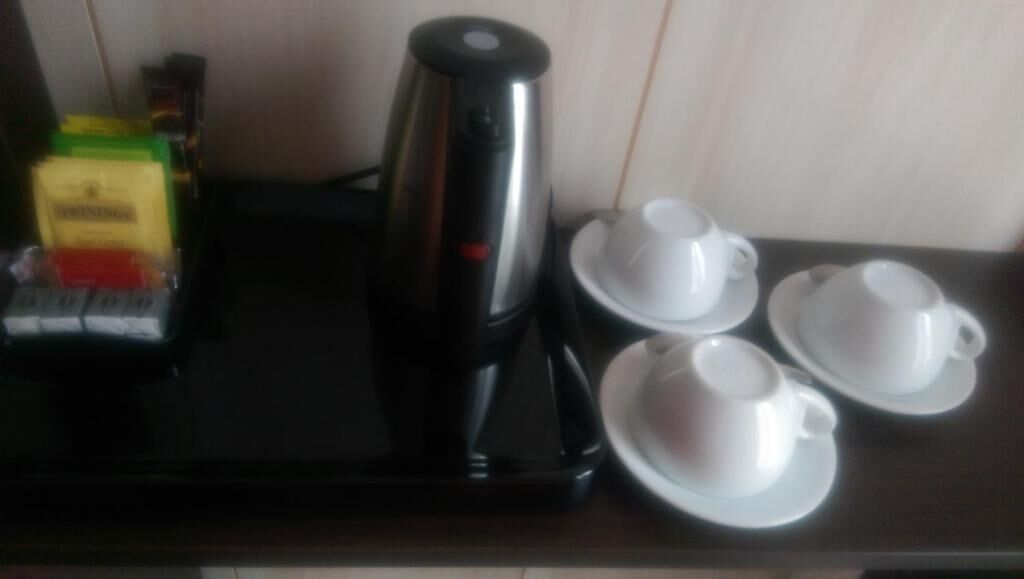 Una cafetera, dos tazas blancas y una caja de café sobre una mesa.