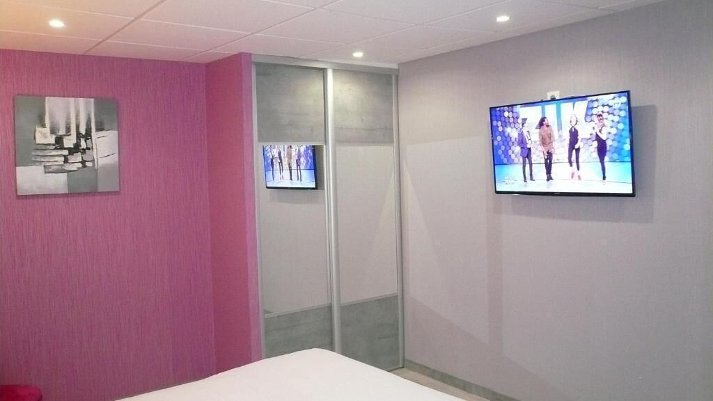 Een hotelkamer met een roze accentmuur, een bed, een televisie aan de muur en een schuifdeur.