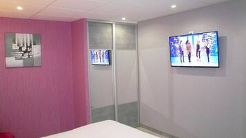 Une chambre d’hôtel avec un mur d’accent rose, un lit, un téléviseur fixé au mur et une porte coulissante.