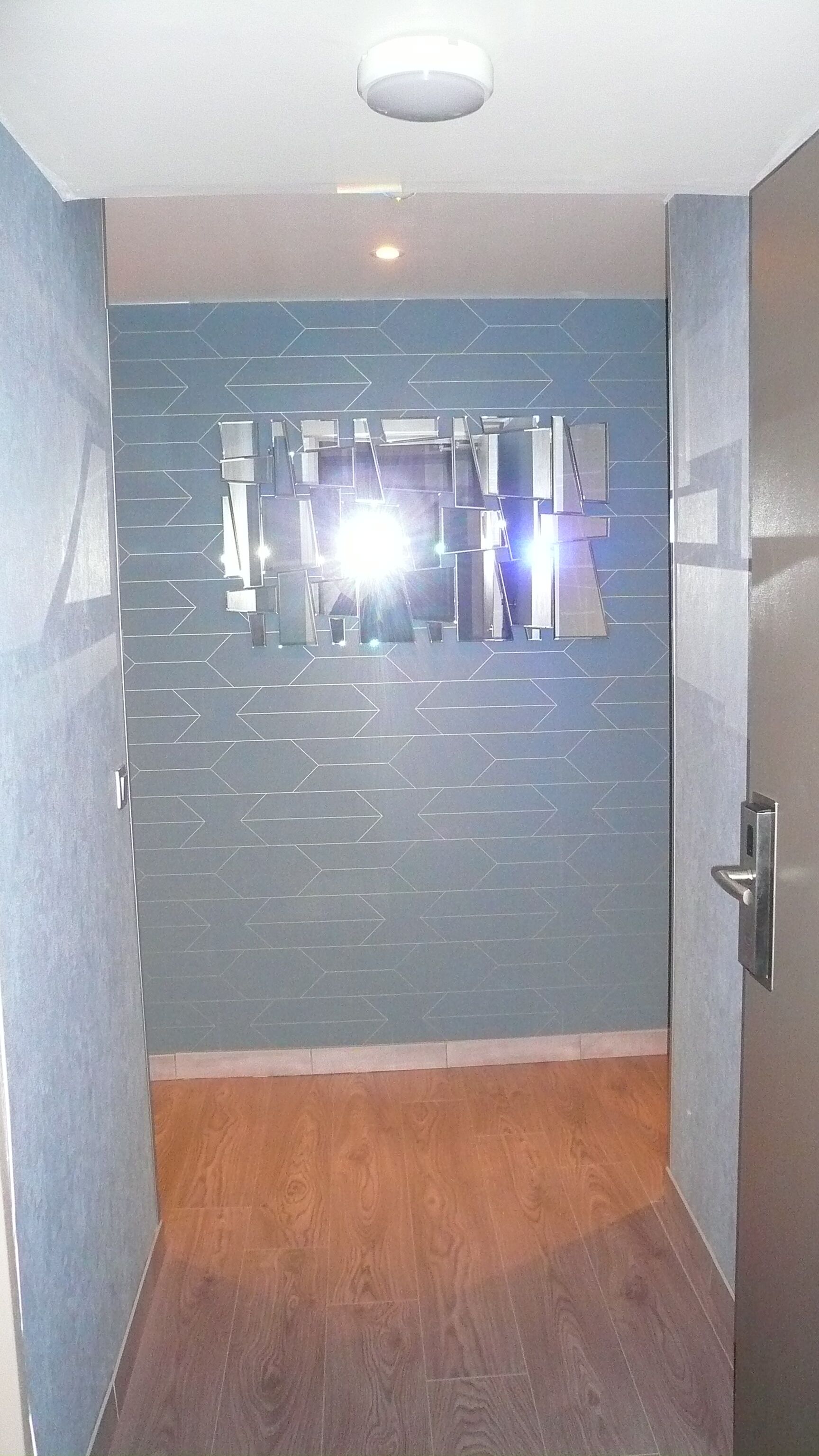 Un pasillo con pared de diseño azul, suelo de madera y una lámpara en el techo.