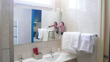 A bathroom with a mirror, two hair dryers, a sink, and towels.